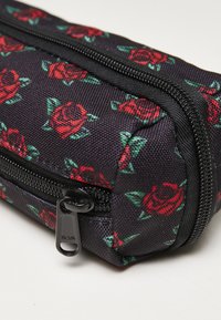 Black fabric pencil case with red rose pattern, featuring a top zipper closure and textured surface for grip. Zipper pull has a circular hole design.
