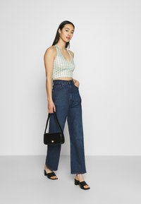 Top cropped em ganga verde e branca com um decote em V profundo, emparelhado com jeans azul-escuro de cintura alta, bolsa preta e sandálias de salto bloco pretas.