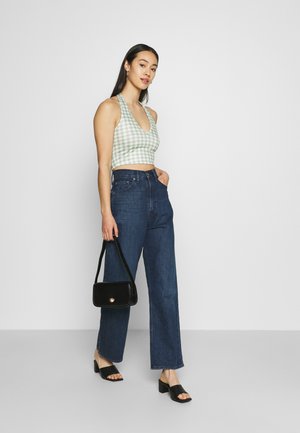 Top cropped em ganga verde e branca com um decote em V profundo, emparelhado com jeans azul-escuro de cintura alta, bolsa preta e sandálias de salto bloco pretas.