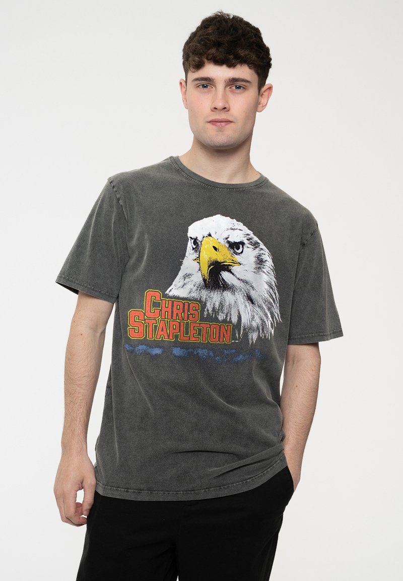 Gray cotton t-shirt featuring an eagle graphic with yellow beak and "CHRIS STAPLETON" text in red. Short sleeves, round neckline, relaxed fit.