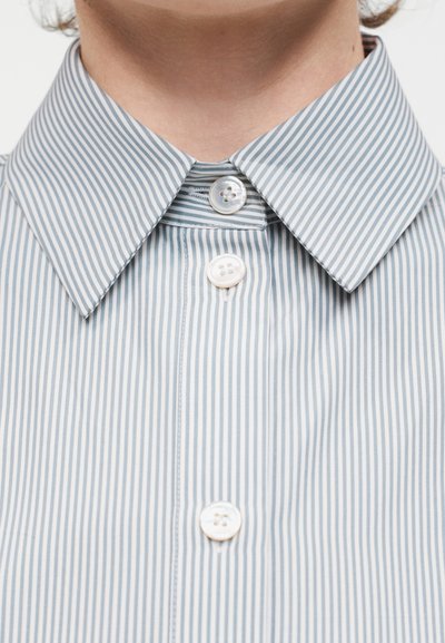 Κοντινό πλάνο γιακά πουκαμίσου με μπλε και λευκές κάθετες ρίγες, κουμπωμένος στην κορυφή με τρία ορατά λευκά κουμπιά μπροστά.