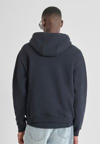 Felpa blu navy in un morbido misto cotone, con cappuccio regolabile, polsini a costine e una vestibilità comoda, abbinata a pantaloni in denim chiaro.