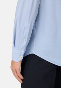 Camicia a righe azzurro chiaro con maniche lunghe, polsini abbottonati e orlo arrotondato. Il tessuto appare liscio con sottili righe strette.