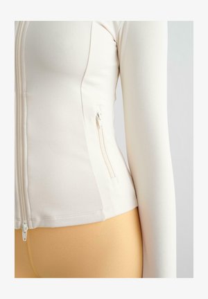 Giacca bianca aderente con zip, realizzata in materiale morbido e elasticizzato. Presenta una tasca laterale con chiusura a zip e maniche lunghe.