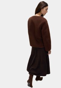 Giacca in pile marrone con una vestibilità ampia, tessuto testurizzato e spalle scese, abbinata a una lunga gonna scura e stivaletti marroni fin sopra il ginocchio.