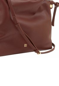 Bruine leren handtas met een gladde textuur, uitgerust met een verstelbare schouderband en een gouden logo-accent aan de zijkant.