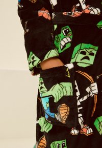 Schwarzer Fleece-Bademantel mit lebhaften Grafiken blockartiger Charaktere. Auffällige Details sind eine Tasche und der weiche, strukturierte Stoff.