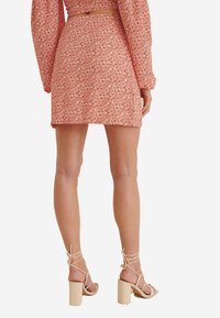 Floral-patterned, knee-length skirt in coral tone, made of textured fabric, paired with beige strappy block-heel sandals.