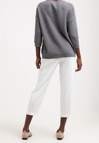Pull gris texturé à manches trois-quarts, associé à un pantalon blanc court. Des chaussures beiges complètent les couleurs neutres de la tenue.