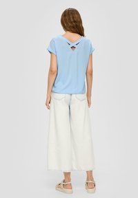 Lichtblauw T-shirt met korte mouwen en een crisscross rugdetail, gecombineerd met wijde lichtblauwe denim broek en beige instapschoenen.