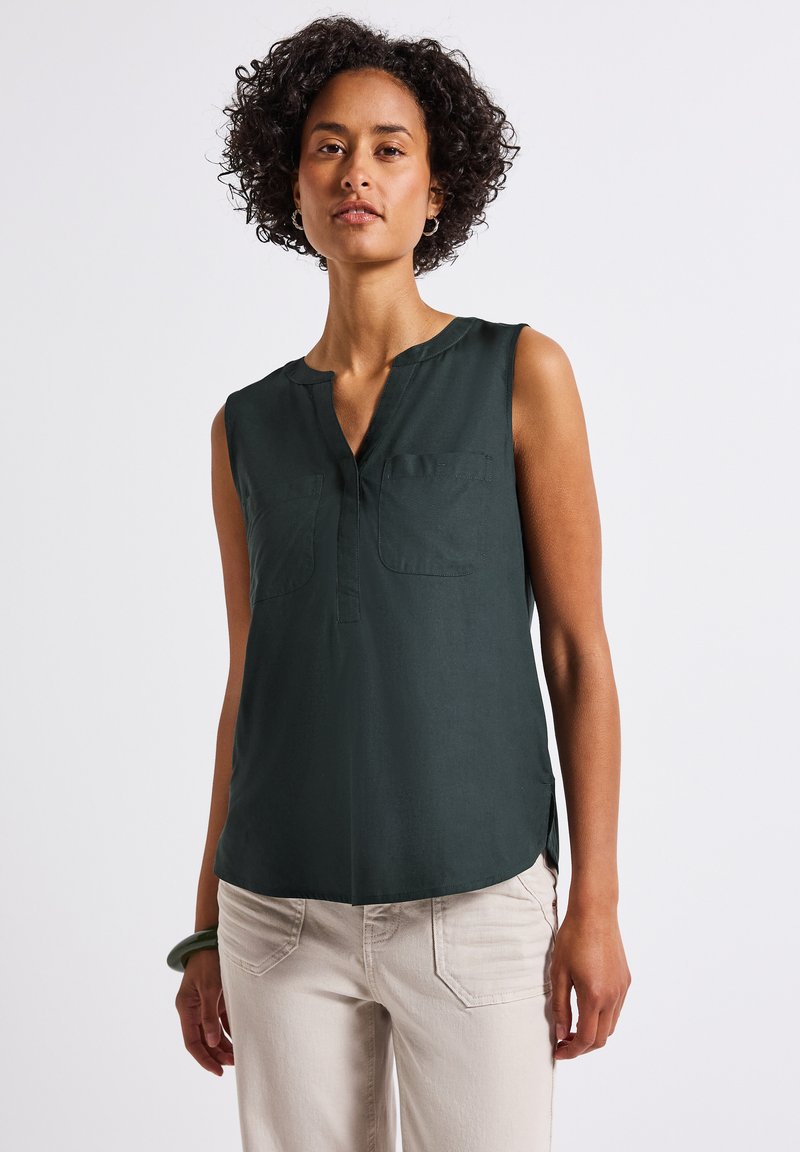 Beżowa bluzka bez rękawów w ciemnozielonym kolorze z dekoltem w serek, dwoma kieszeniami na piersi oraz delikatnym rozcięciem z boku. Wykonana z gładkiego materiału, świetnie komponuje się z jasnymi spodniami.