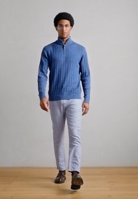 Μπλε πουλόβερ με πλέξη καναλιών και ψηλό γιακά, ανοιχτό γκρι παντελόνι και καφέ παπούτσια. Ομαλή υφή, εφαρμοστή σχεδίαση και μεσαίο μήκος.