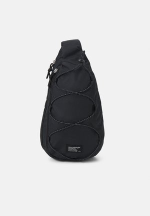 Czarna torba na ramię w kształcie kropli z przednim szczegółem z linką bungee, kieszenią na zamek i naszywką z logo Levi Strauss na dole na środku.