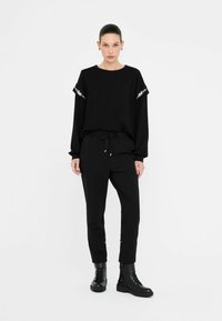 Top nero a maniche lunghe con dettagli decorativi sulle maniche, abbinato a pantaloni neri con elastico in vita e stivali neri stringati.