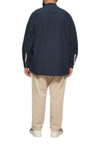 Marineblaue langärmlige Bluse mit einem Rückensattel-Detail und Schlitzen an den Bündchen, kombiniert mit beigefarbenen Cordhosen und weißen Sneakers.
