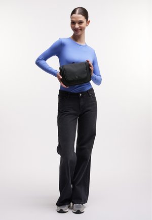 Schwarze Stofftasche mit Klappenverschluss, glatter Textur, rechteckiger Form und kleinem Logo auf der Vorderseite, in den Händen einer Person gehalten.