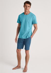 Turquoise katoenen T-shirt met een klassieke ronde hals, gecombineerd met blauwe shorts met een patroon van witte stippen, ontworpen voor casual draag. 