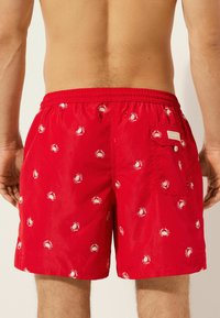 Rote Schwimmshorts aus leichtem Material mit einem weißen Krebsdesign, elastischem Bund und einer Gesäßtasche mit Etikett.