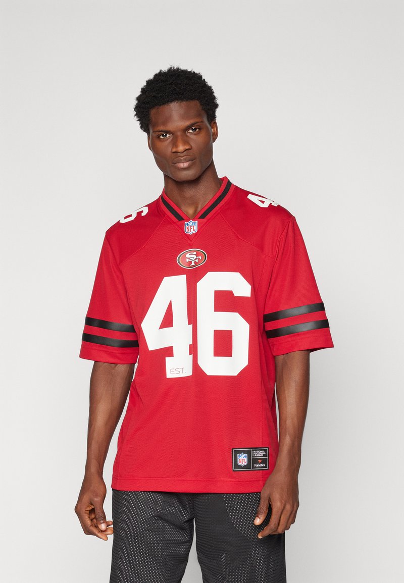 Sarkanais NFL krekls ar melnām svītrām uz piedurknēm, skaitlis "46" baltā krāsā, komandas logo uz krūts, izgatavots no elpojoša materiāla. Zem tā redzami melni šorti.