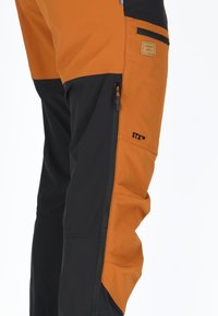 Utomhusbyxor med en svart nederdel och en orange överdel, utrustade med en ficka med dragkedja och ett märkespatch på sidan.