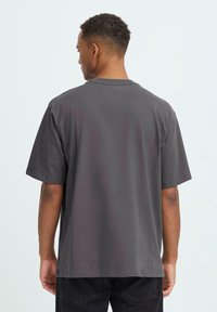 T-shirt in cotone grigio con maniche corte, colletto rotondo, vestibilità rilassata e design semplice. Il tessuto appare morbido con una texture liscia.
