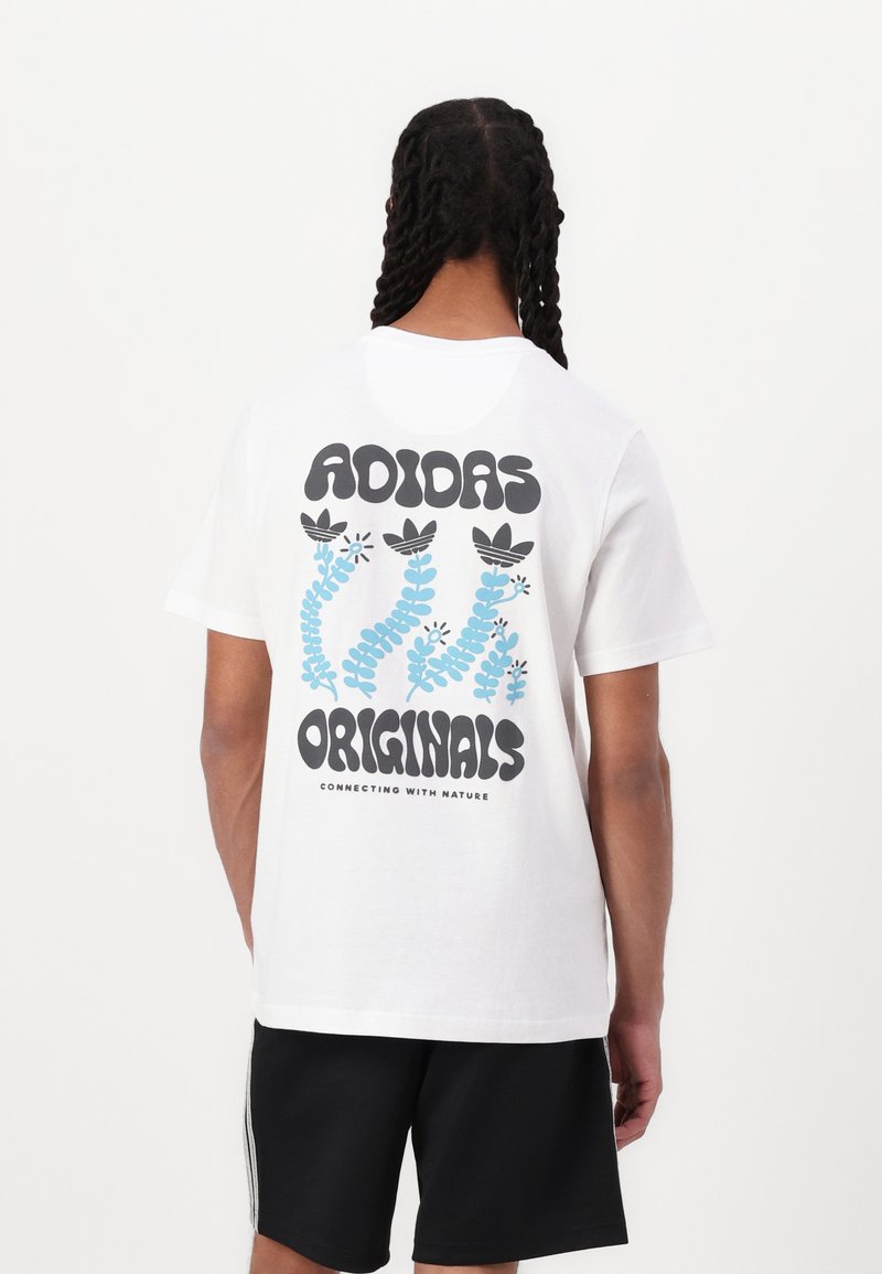 White cotton t-shirt featuring large black text and blue floral graphics on the back, with "ADIDAS ORIGINALS" and tagline at the bottom.