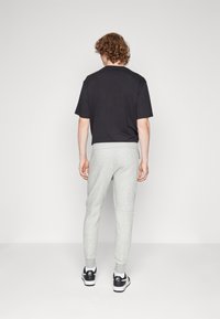 T-shirt nero a maniche corte abbinato a pantaloni felpa grigi chiari a gamba affusolata, con polsini a costine e vita con cordoncino. Sneakers nere.