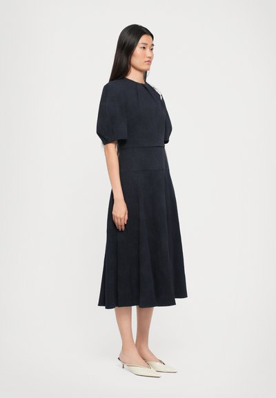 Navyblauwe jurk met korte, gezwollen mouwen en een aansluitend lijfje. Glad textuur, A-lijn silhouet en subtiel patroon door de hele jurk.