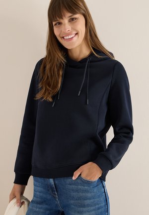 Marineblauwe hoodie met trekkoorden, ribgebreide manchetten en zoom. Gecombineerd met lichtblauwe spijkerbroek. Gladde textuur, casual ontwerp.
