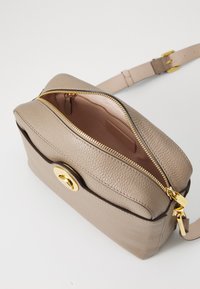 Bežana kožna torba za crossbody sa teksturiranom površinom, zlatnim zatvaračem i hardverom, te preklopom. Unutrašnjost je svijetlosmeđa s zip džepom.