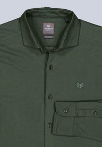 Dunkelgrünes Pima-Baumwollhemd mit Knopfleiste, spitzem Kragen, linker Brusttasche und einem dezenten Logo, das über der Tasche gedruckt ist.