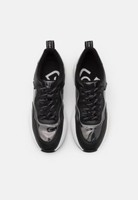 Chaussures de sport noires avec une tige en mesh noir et gris brillant, un col rembourré, des lacets noirs et une semelle blanche texturée. Logo de la marque sur la languette.