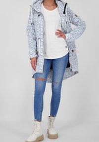 Wodoodporny płaszcz w niebieskie kropki, na białym tle, z regulowanym kapturem, przednimi kieszeniami, zestawiony z białym T-shirtem i przetartymi niebieskimi dżinsami.