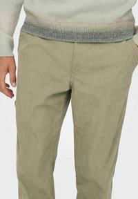 Beige fløjlsbukser med lodret ribbning, der har sidelommer og en afslappet pasform, parret med en gradient striktrøje.