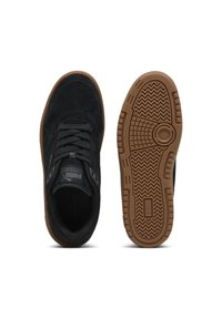 Svarta mockaskor med en gummitå skor i brunt, med en rund logotyp på tungan och mönstrad sula för grepp. Visade från ovan och under.