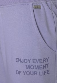 Paarse katoenen sweats met zijzakken, voorzien van een vet gedrukt slogan "GENIET VAN ELK MOMENT VAN JE LEVEN" in donkergrijs. Inclusief metalen logo-detail.