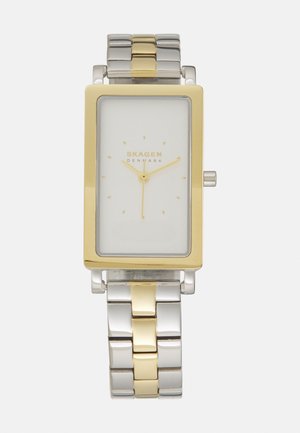 Stačiakampis laikrodis su baltu ciferblatu, auksinės spalvos rėmeliu ir sidabro bei aukso spalvos metaliniu grandinėliu. Minimalistinis dizainas su paprastais valandų žymekliais.