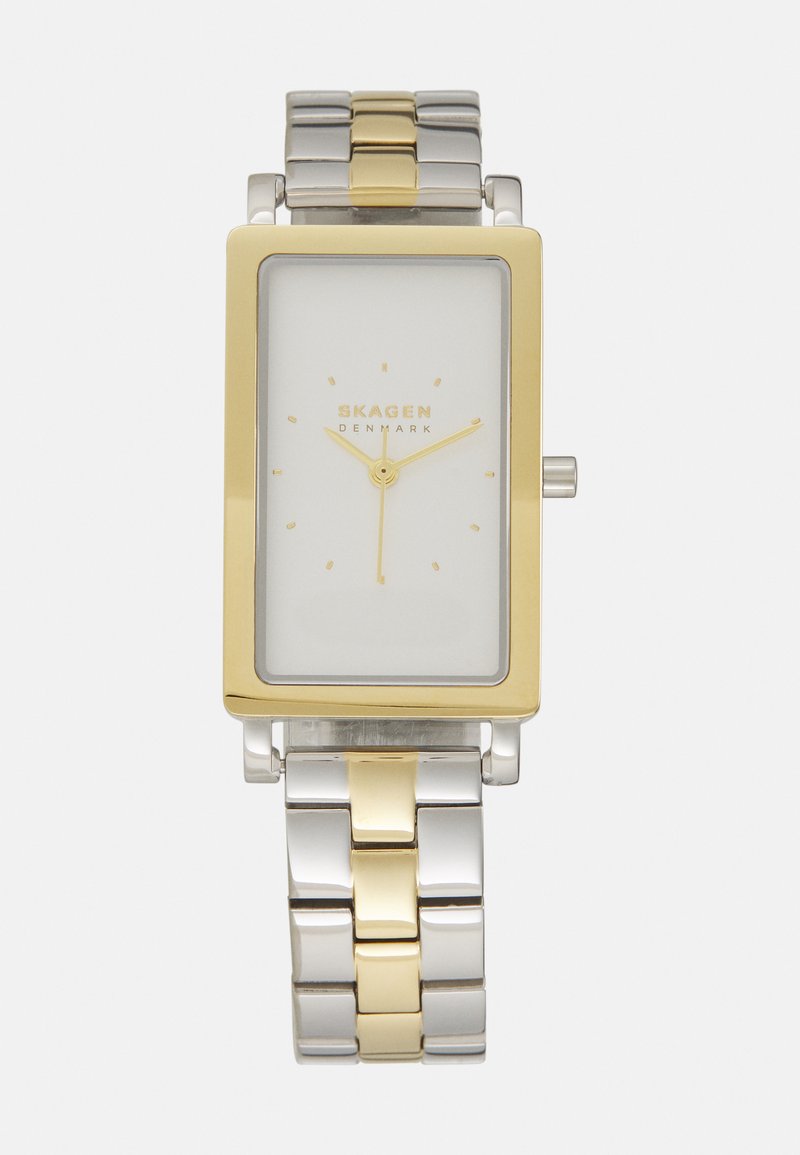 Rektangulär klocka med en vit urtavla, guldfärgad bezel och armband av silver- och guldfärgade metalplankor. Minimalistisk design med enkla timmarkörer.