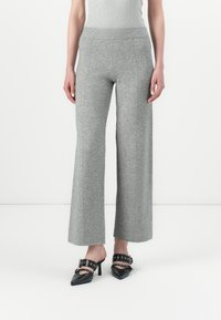 Pantaloni grigi a gamba larga realizzati in tessuto morbido con cuciture visibili. Abbinati a scarpe nere con tacco dotate di aperture e accenti circolari.