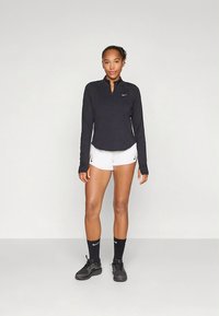 Melns, ar garām piedurknēm, sportisks tops ar rāvējslēdzēju, kopā ar baltām šortiem. Valkāts ar melnām sporta kurpēm un zeķēm ar nelielu logotipu.