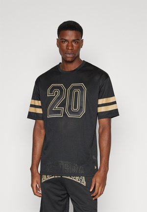 Maglia in mesh nera con accenti dorati, con il numero "20" in evidenza sul davanti e dettagli a righe sulle maniche.