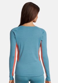 Maglietta a maniche lunghe con un corpo blu e accenti di rete corallo sui lati, realizzata in un tessuto morbido ed elasticizzato, con scollatura a girocollo.