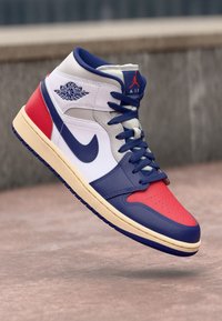 Sneaker alta con pannelli in pelle rossi, bianchi e blu, dettagli testurizzati e punta perforata. Presenta il logo iconico e una suola crema.