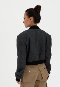 Harmaa herringbone-kuosiset pommitakki mustilla ribbikauluksilla ja -hihoilla. Sopiva mittasuhde, lyhyt pituus, teksturoitu kangas.