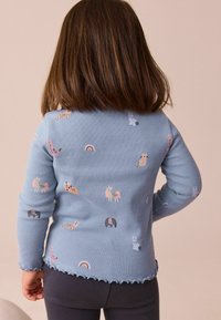 Blau gestreiftes Langarmoberteil mit bunten Tier- und Regenbogenmustern, gewelltem Saum und taillierter Passform. Kombiniert mit dunklen Leggings.