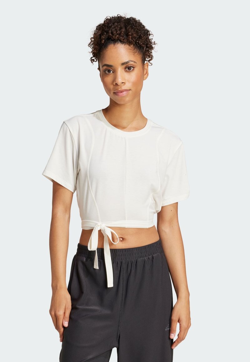 Top corto de manga corta en suave tela blanca con cuello redondo y detalle de nudo en la parte delantera. Combinado con pantalones negros con pliegues.