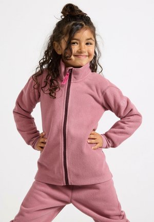 Giacca in pile rosa con zip e colletto alto, caratterizzata da una zip a contrasto. Tessuto morbido. Bambino in posa con le mani sui fianchi.