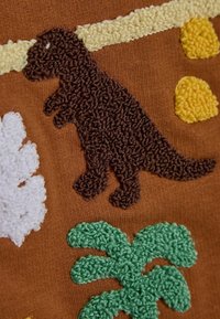 Hnědá látka s texturovanou výšivkou dinosaura v tmavě hnědé, žlutých tvarech, bílé foliaci a zelenými palmami.