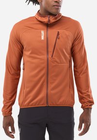 Veste zippée orange avec col montant, design ajusté, tissu texturé et poches zippées. Présente un logo sur la poitrine et des coutures discrètes.