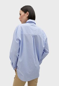 Camicia button-up in tessuto a righe blu chiaro, caratterizzata da sottili motivi ricamati e una vestibilità rilassata. Maniche lunghe con bottoni ai polsini.